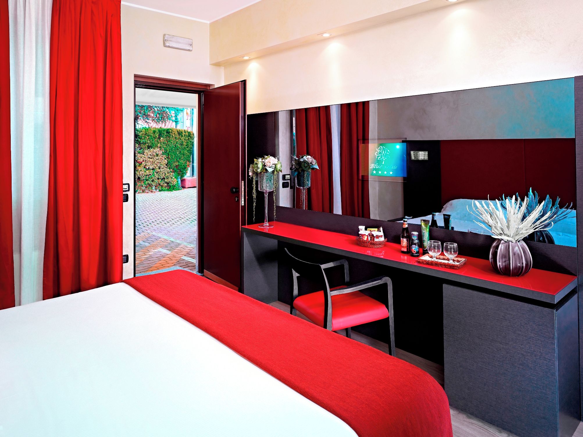 Une chambre d’hôtel avec un lit, un bureau, une chaise, un miroir et une fenêtre avec des rideaux.