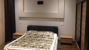 Ett sovrum med en säng, sängbord, en tv som är monterad på väggen och en garderob.
