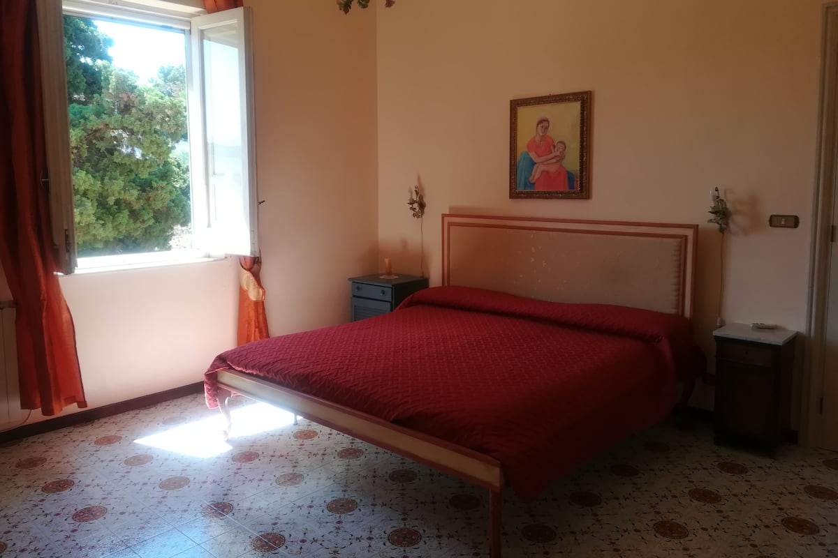 A bedroom with a bed, a nightstand, a window with curtains, a wall-mounted picture, and a patterned floor.