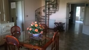 Un comedor con una mesa de vidrio, sillas y un centro de mesa floral. Se ve una escalera de caracol al fondo.