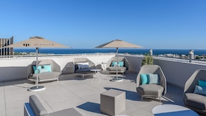 A rooftop terrace with outdoor seating, umbrellas, and a view of the ocean.