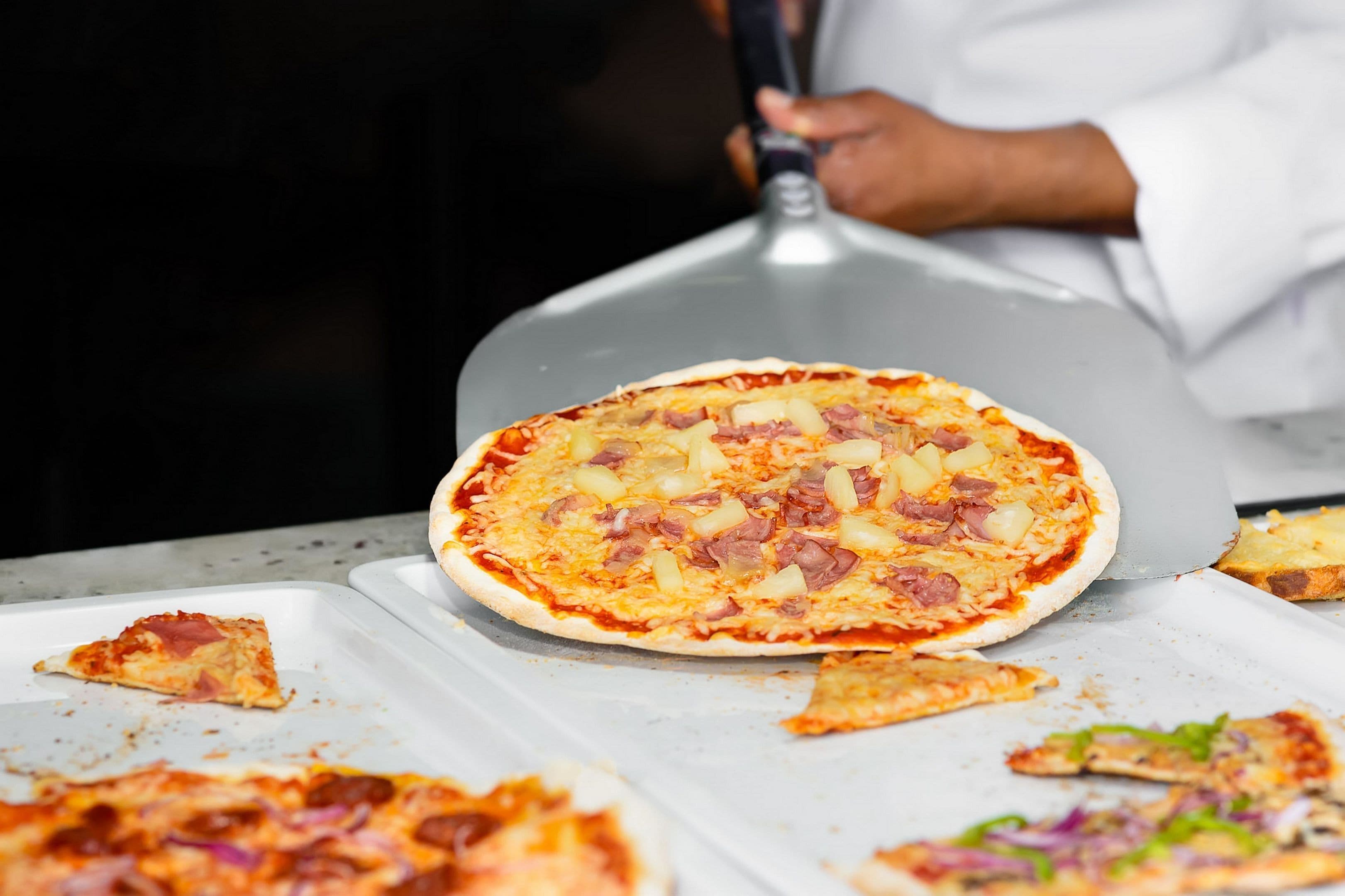 Una pizza con jamón y piña sobre una bandeja de metal.