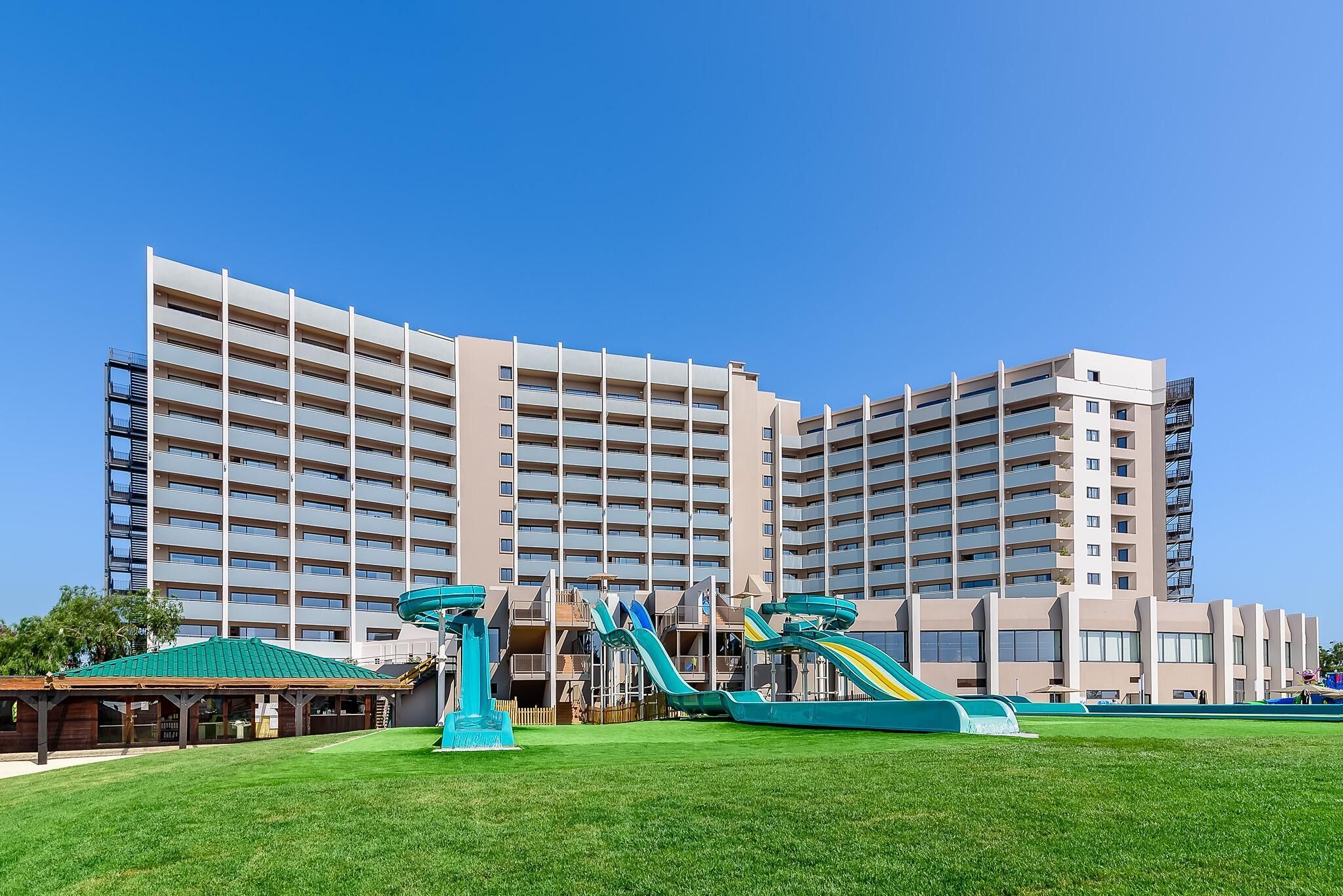 Un hôtel à plusieurs étages, doté d’un toit plat, de grandes fenêtres et d’une pelouse verdoyante avec des jeux pour enfants.