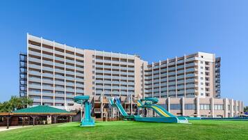 Un hôtel à plusieurs étages, doté d’un toit plat, de grandes fenêtres et d’une pelouse verdoyante avec des jeux pour enfants.