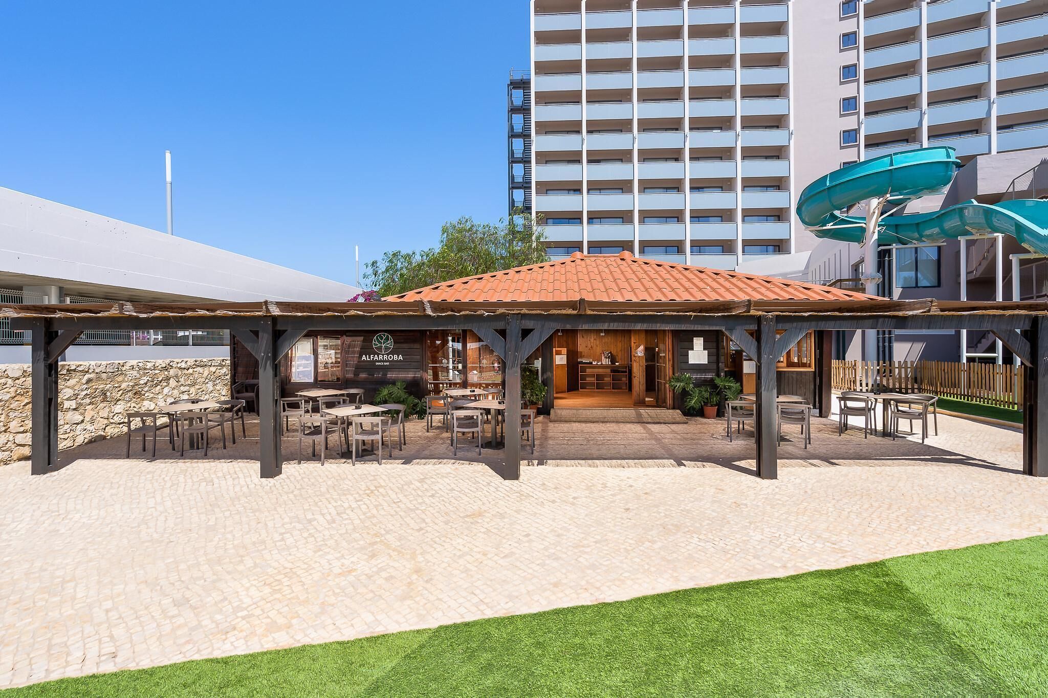 An outdoor patio area with tables and chairs, a covered seating area, and a water slide structure.