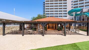 An outdoor patio area with tables and chairs, a covered seating area, and a water slide structure.