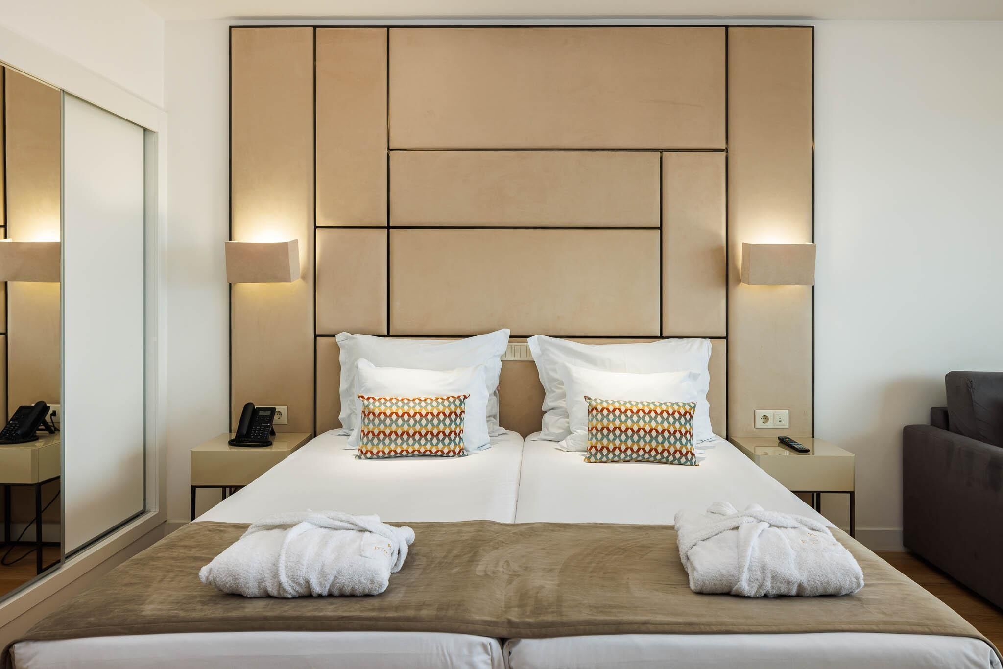 A hotel room with a large bed, two bedside tables, a mirror, a sofa, and a wall-mounted headboard.