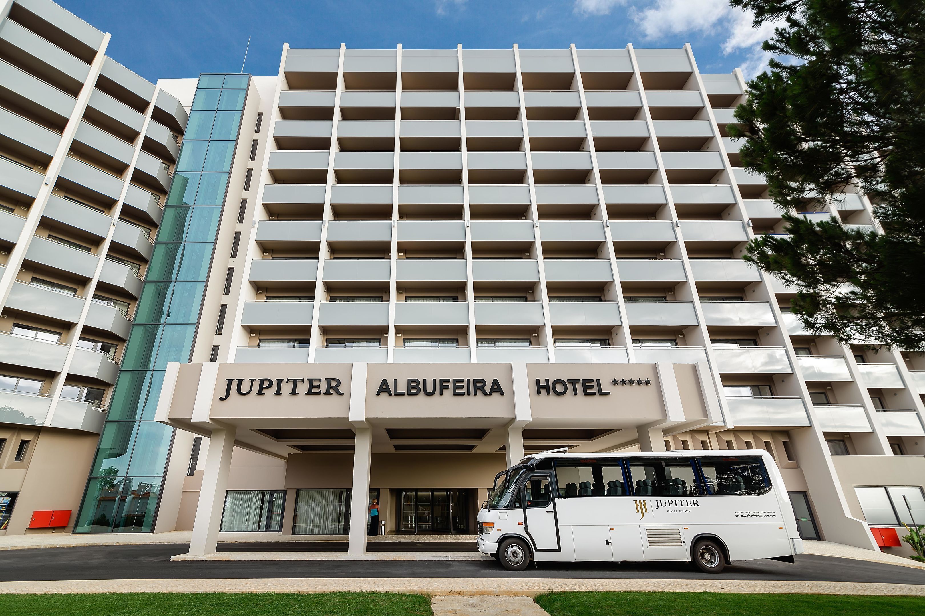 A multi-story hotel with a modern design, featuring a prominent entrance and a bus parked in front.