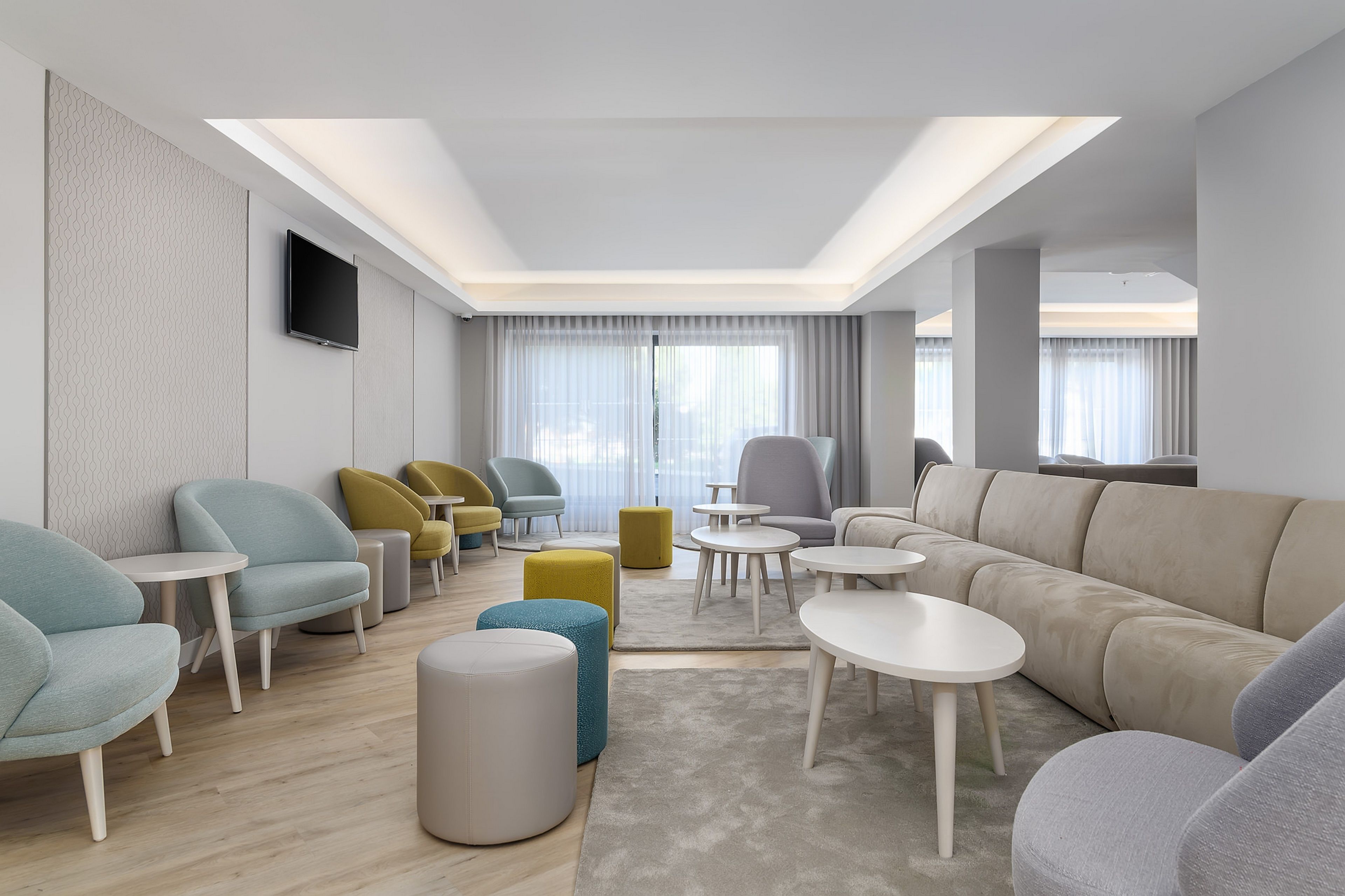 Una sala de estar moderna con un sofá, sillones, otomanas y un televisor de pantalla plana montado en la pared.