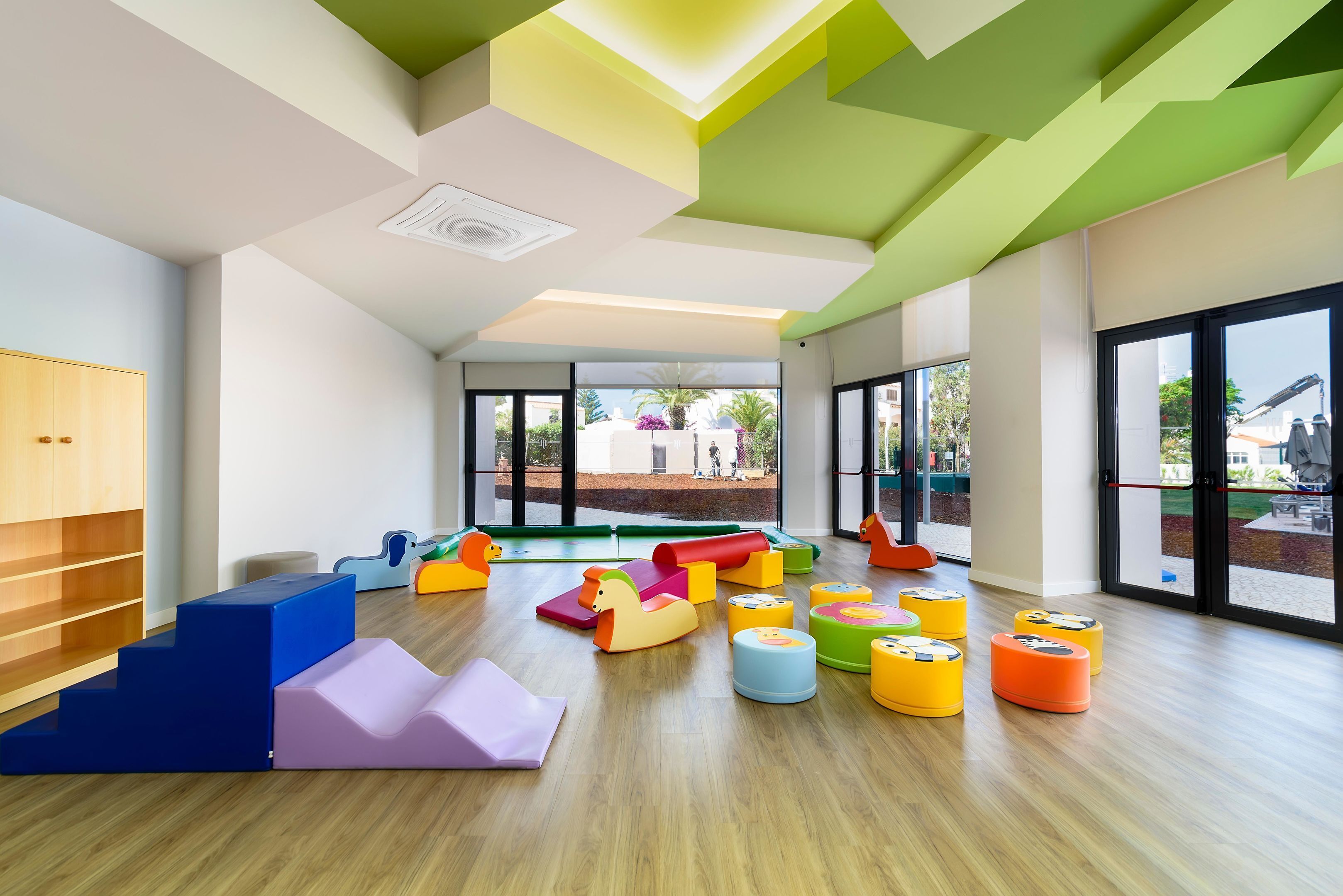 A brightly lit indoor play area with colorful play structures and large windows.