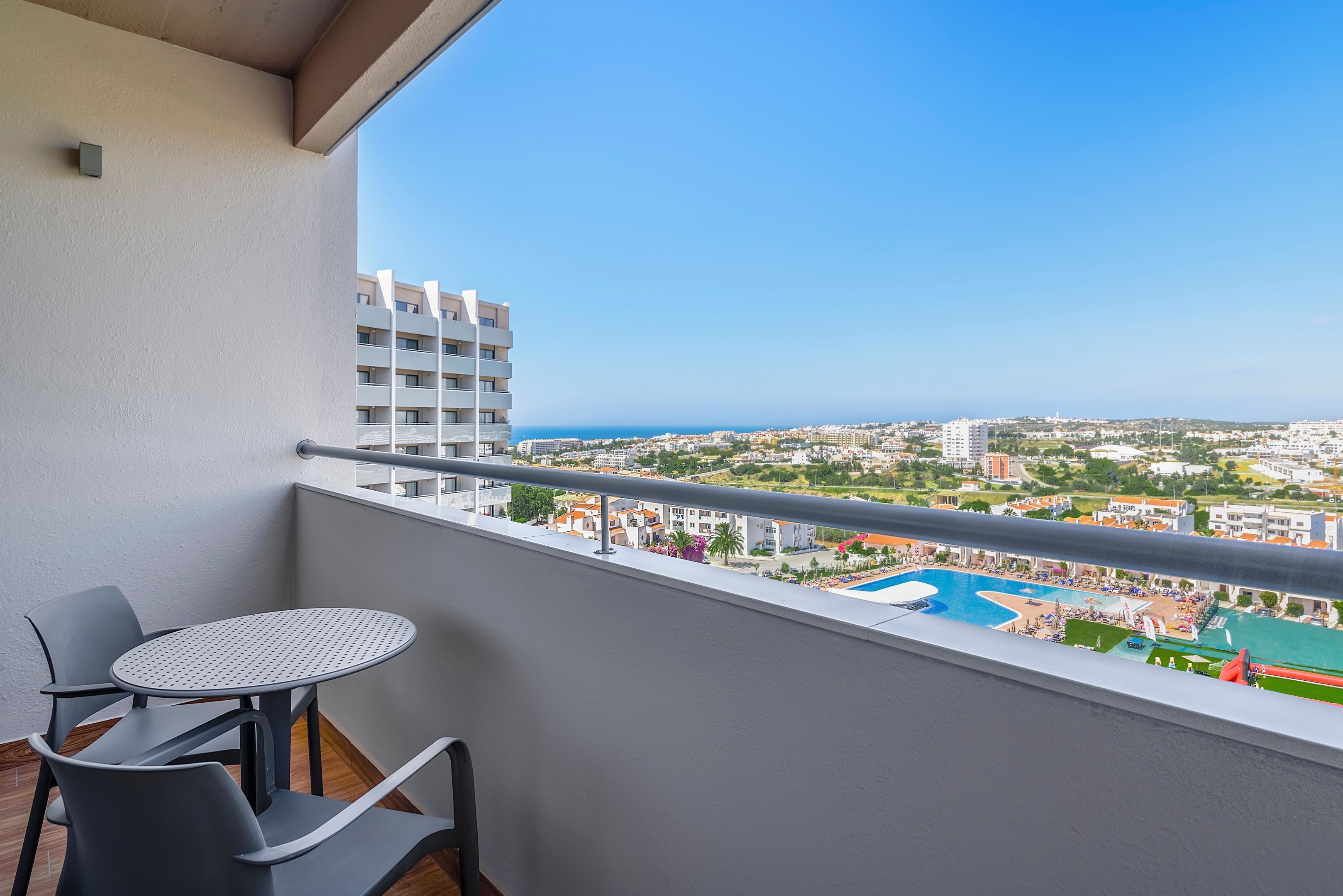 A balcony with a table and chairs, overlooking a cityscape and a swimming pool.
