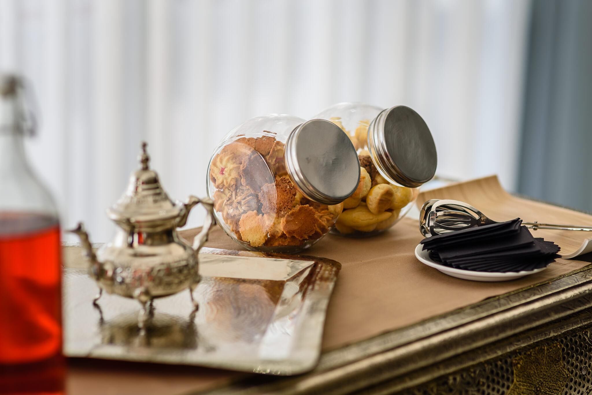 Un plateau avec un bocal en verre rempli de biscuits, une théière en métal et une assiette avec des serviettes.