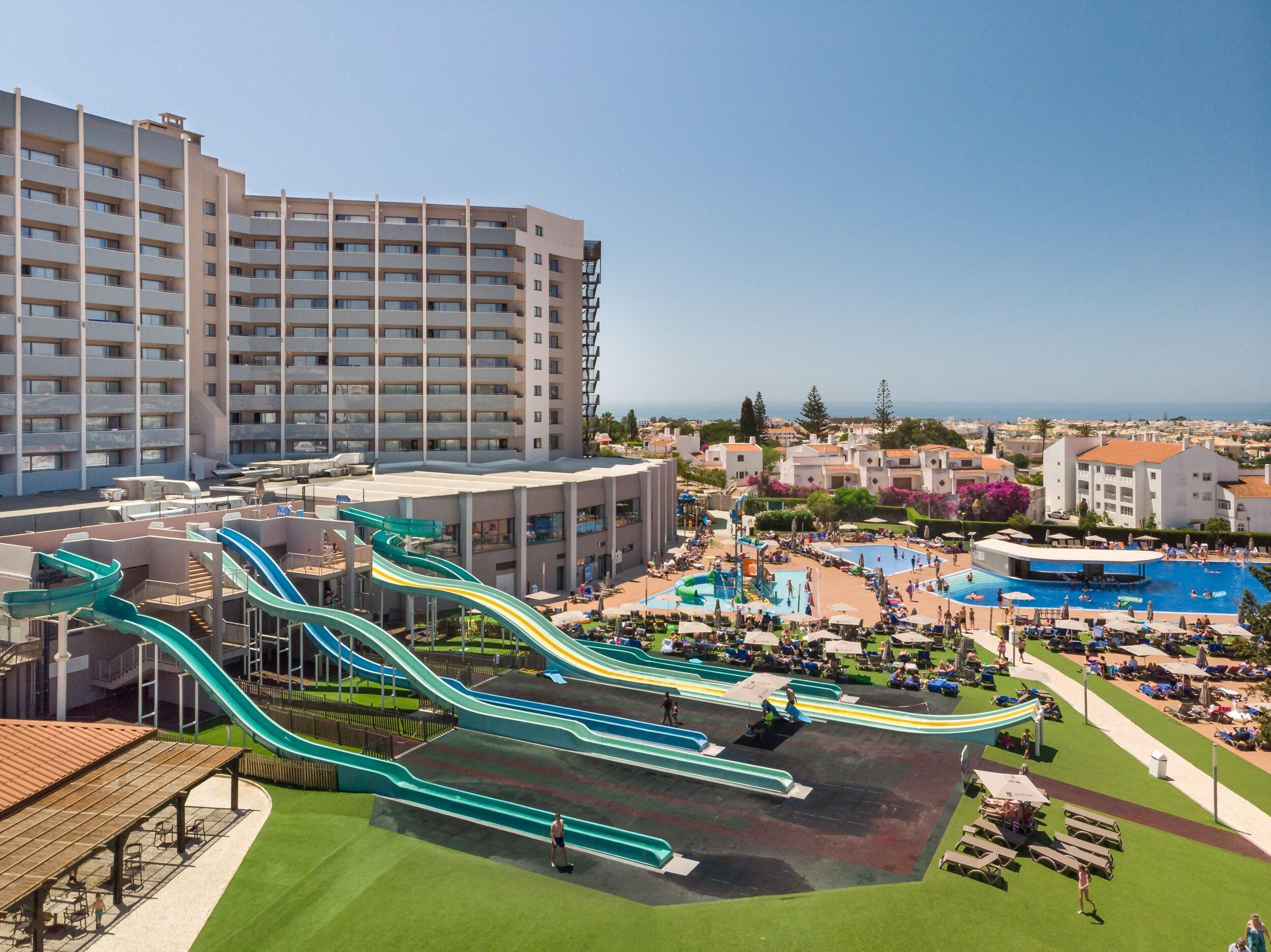 A resort with multiple swimming pools, a large water park with slides, and a view of the sea.