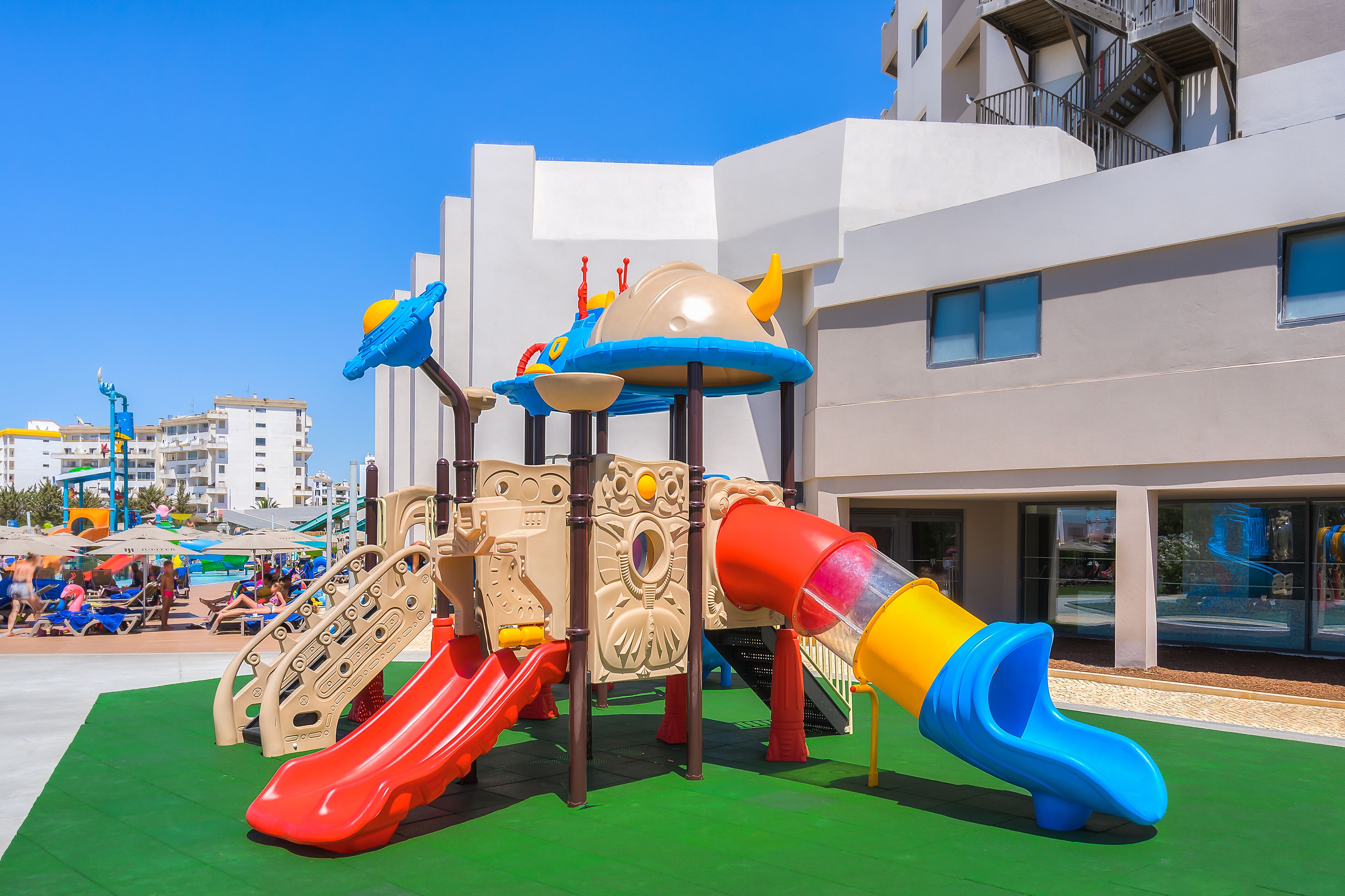 Un patio de juegos con toboganes y estructuras para escalar, frente a un edificio moderno con balcones.