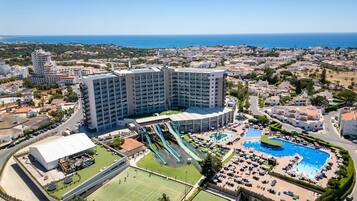 Un hotel grande con múltiples piscinas, una cancha deportiva y vistas al mar.