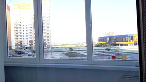 A view through a window of a multi-story building with a parking lot and a large commercial building in the background. - Apartments on Prospekt Dzerzhinskogo 240 (Novorossijsk)