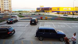A parking lot with several cars, a playground, and a building with a yellow and blue facade. - Apartments on Prospekt Dzerzhinskogo 240 (Novorossijsk)