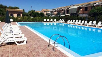 Una piscina con sillas de descanso blancas y un suelo de baldosas.