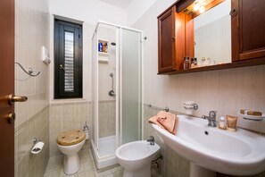 A bathroom with a toilet, bidet, shower, sink, and wooden cabinet. - Agave Residence (Campofelice di Roccella)