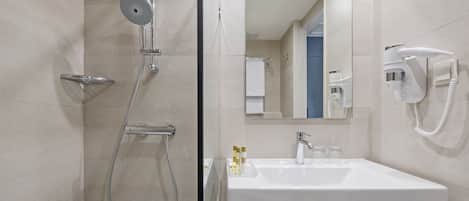 Un baño moderno con ducha de vidrio, lavamanos blanco y secador de pelo montado en la pared.