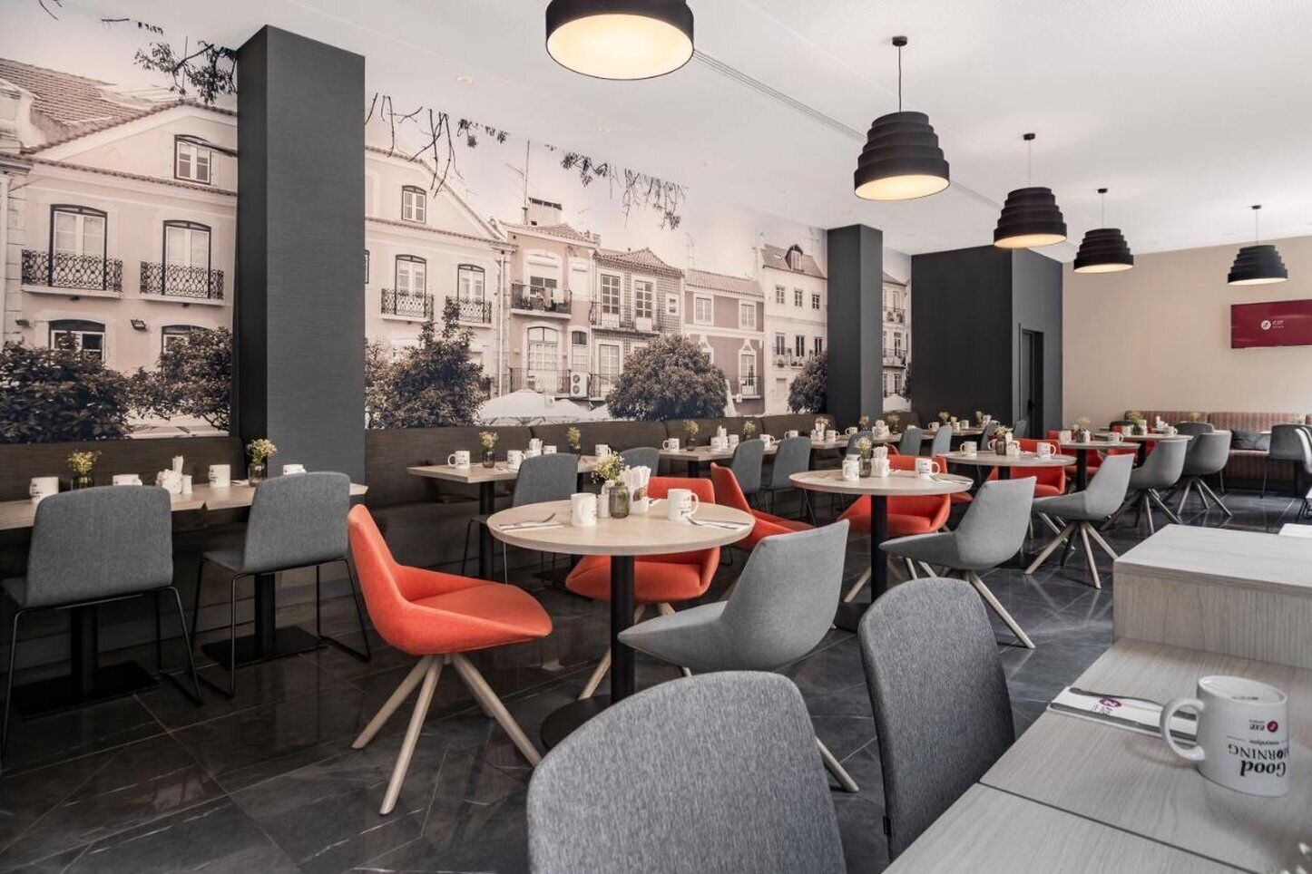 A modern cafe with round tables and chairs, a mural of buildings, and pendant lighting.