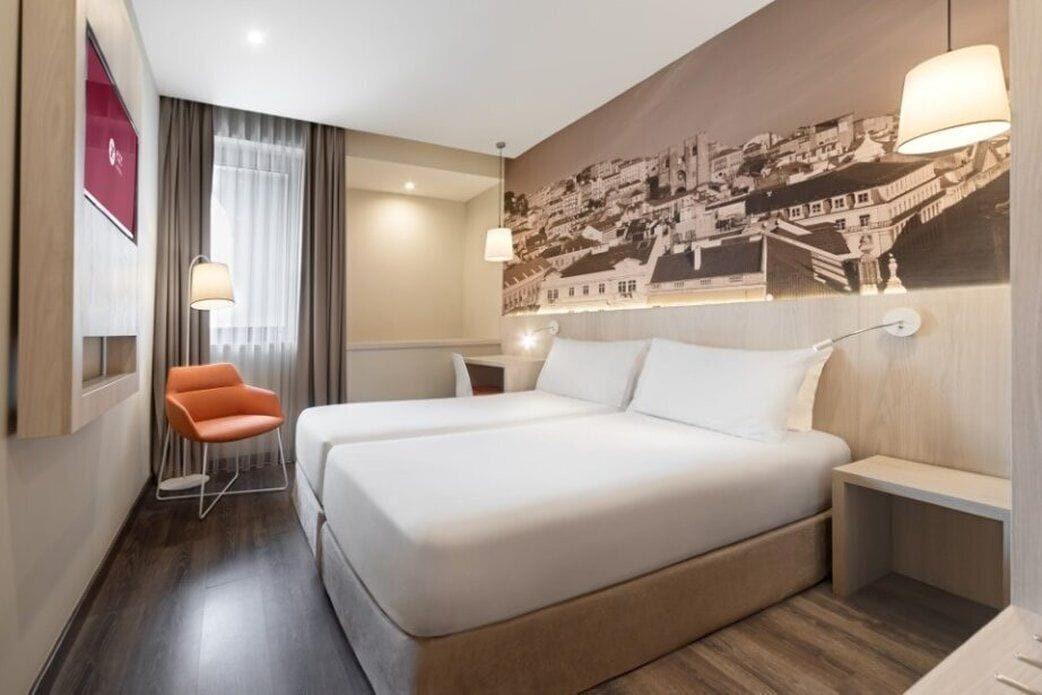Une chambre d’hôtel avec un grand lit, une chaise, un bureau et une lampe fixée au mur.