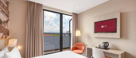 Ein Hotelzimmer mit Bett, Schreibtisch, Stuhl, Fernseher und Blick auf die Stadt durch das Fenster.