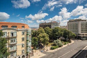 Vista de una calle con una mezcla de edificios residenciales y comerciales, incluyendo un edificio blanco destacado con techo rojo y una amplia zona arbolada.