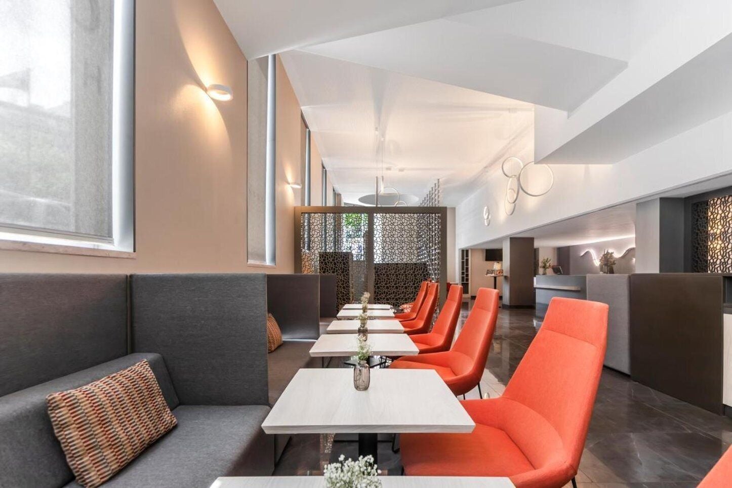 Un restaurant moderne avec de hauts plafonds, une grande salle à manger avec des chaises orange et un coin salon confortable avec des canapés gris.