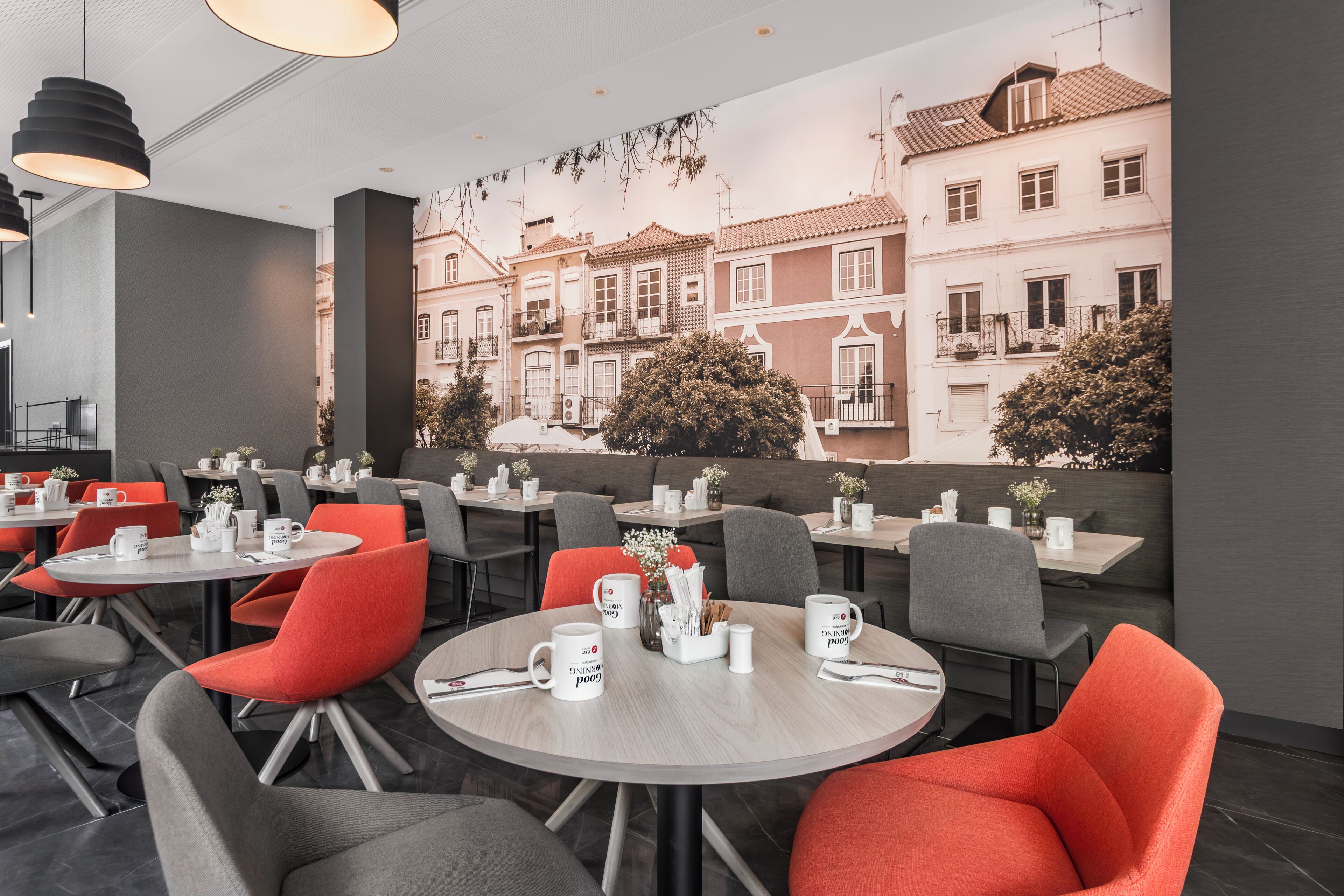 A modern cafe with round tables and chairs, some with orange cushions.