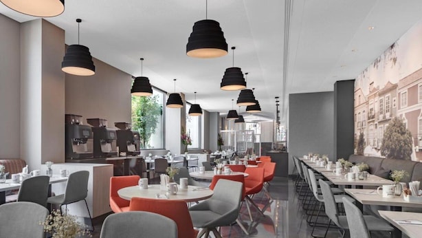 A modern restaurant with round tables, black pendant lighting, and a cityscape mural on the wall. - Dorma Liberdade (Lisbon)