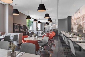 A modern restaurant with round tables, black pendant lighting, and a cityscape mural on the wall.