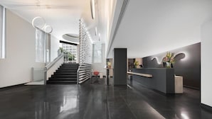 A modern reception area with a staircase leading to upper floors, a reception desk, and a glass partition. - Dorma Liberdade (Lisbon)