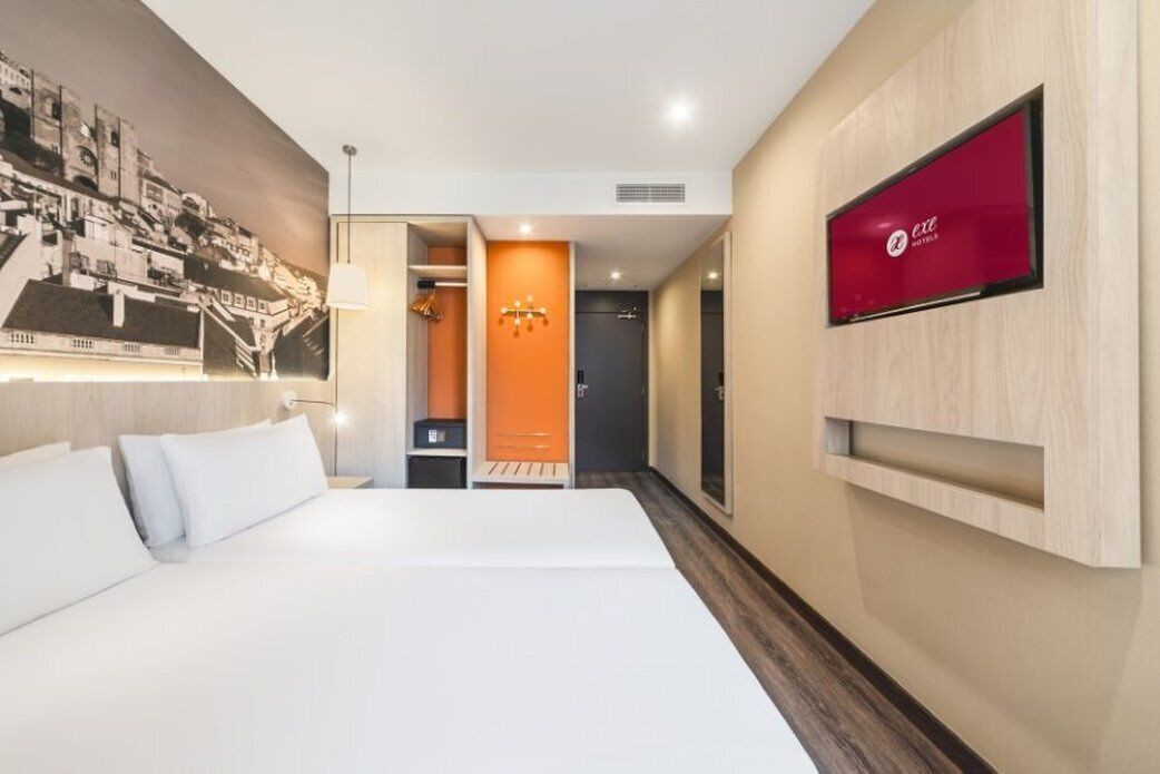 A hotel room with a large bed, a TV mounted on the wall, and a mural of a cityscape.