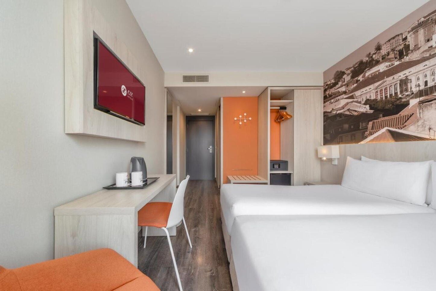 A hotel room with a bed, a desk with a chair, a television, and a painting of a cityscape.