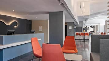 Um saguão de hotel moderno com uma mesa de recepção, assentos laranja e uma área de bar.