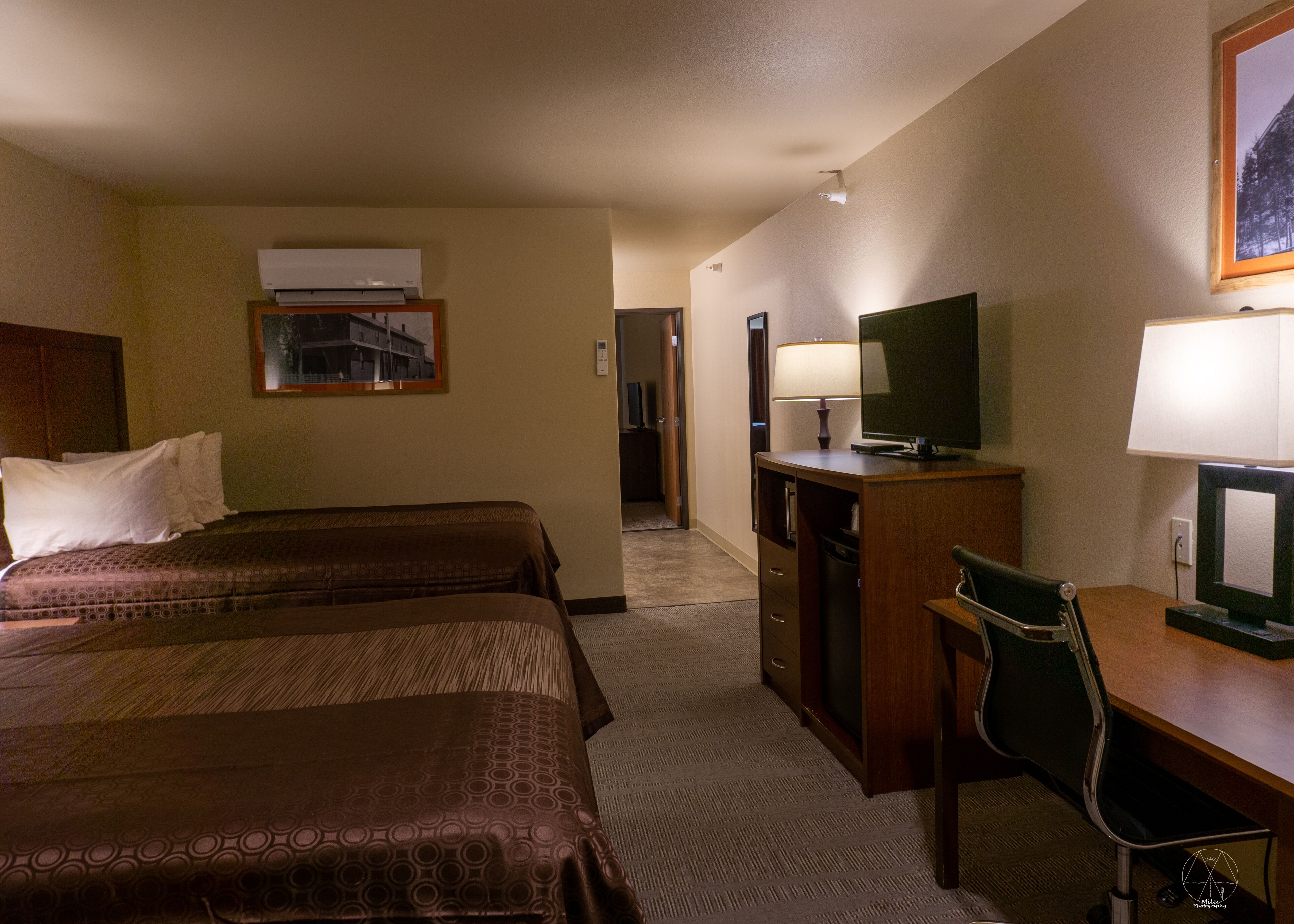 A hotel room with two beds, a desk with a computer, a lamp, and a television.