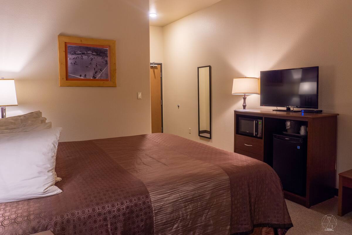 A hotel room with a bed, a television, a microwave, and a mirror.