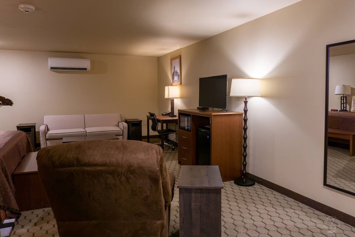 A hotel room with a sofa, a desk with a computer, a flat-screen TV, a lamp, and a mirror.