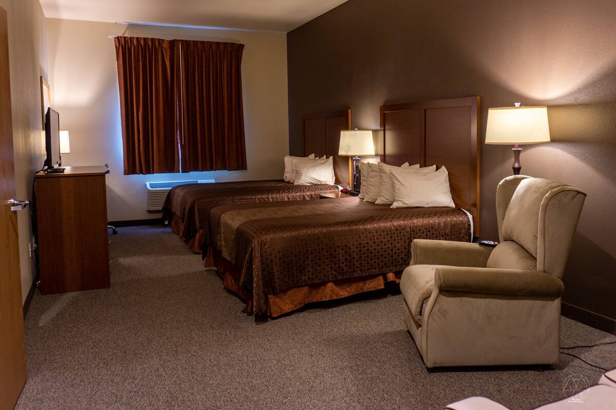 A hotel room with two beds, a desk, a chair, and a window with curtains.