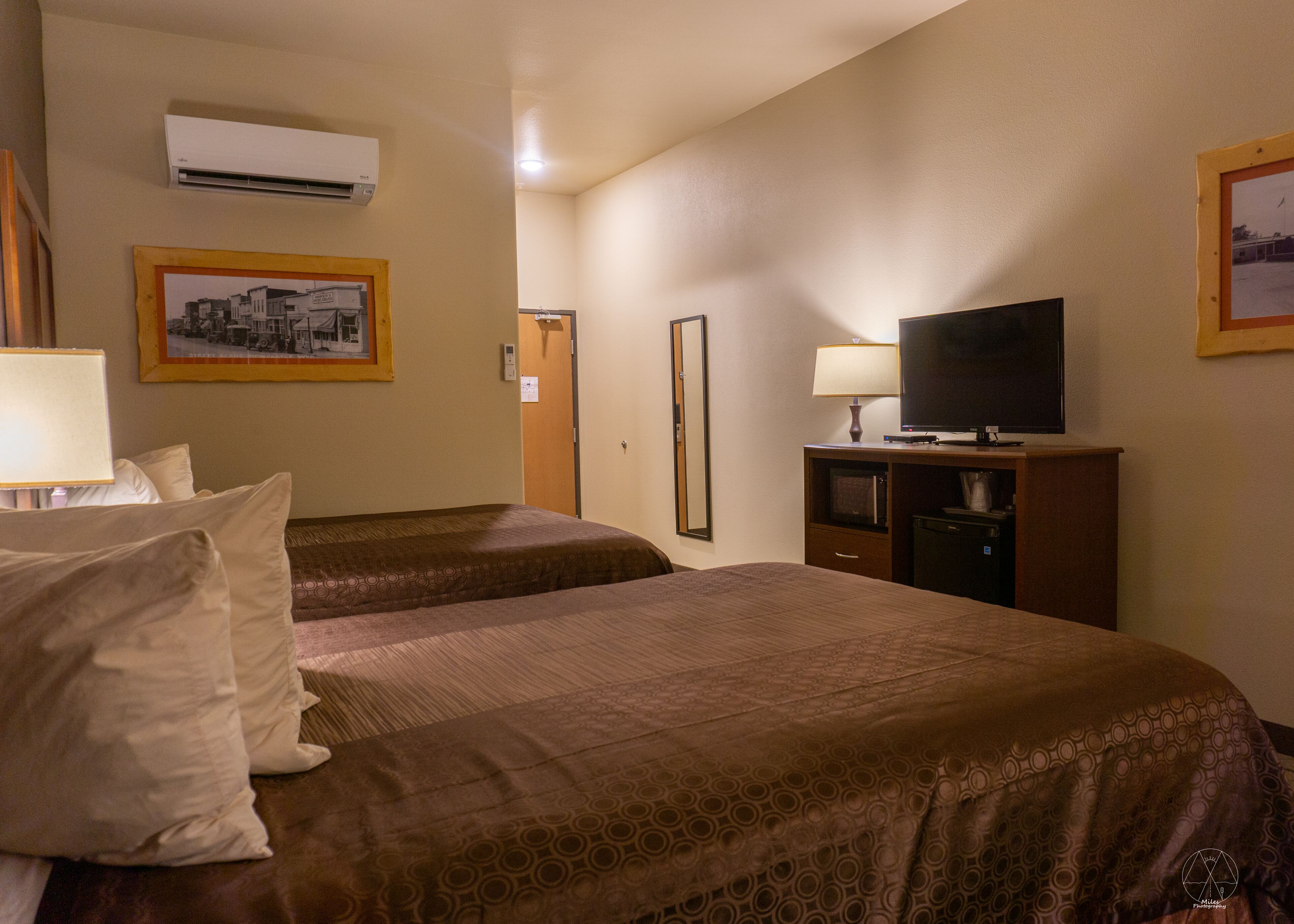 Quarto de hotel com duas camas, televisão, escrivaninha com luminária e ar condicionado.