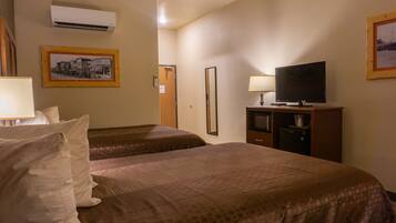 Quarto de hotel com duas camas, televisão, escrivaninha com luminária e ar condicionado.
