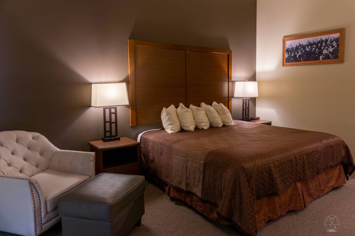 A hotel room with a large bed, two bedside tables with lamps, a chair, and an ottoman.
