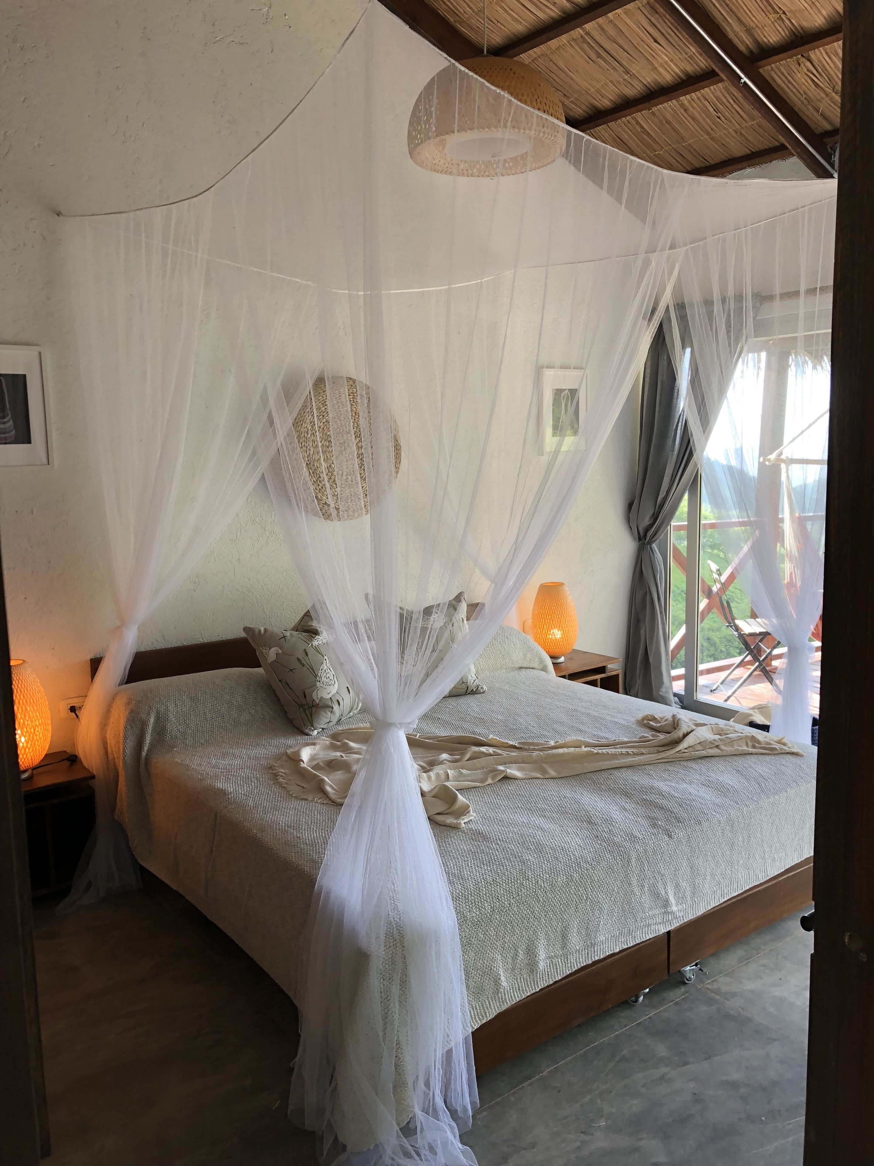 Un dormitorio con cama con dosel, una lámpara de noche y vistas al exterior.
