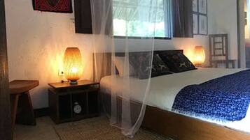 Un dormitorio con una cama cubierta por una mosquitera, dos lámparas de noche, un reloj y un taburete de madera.