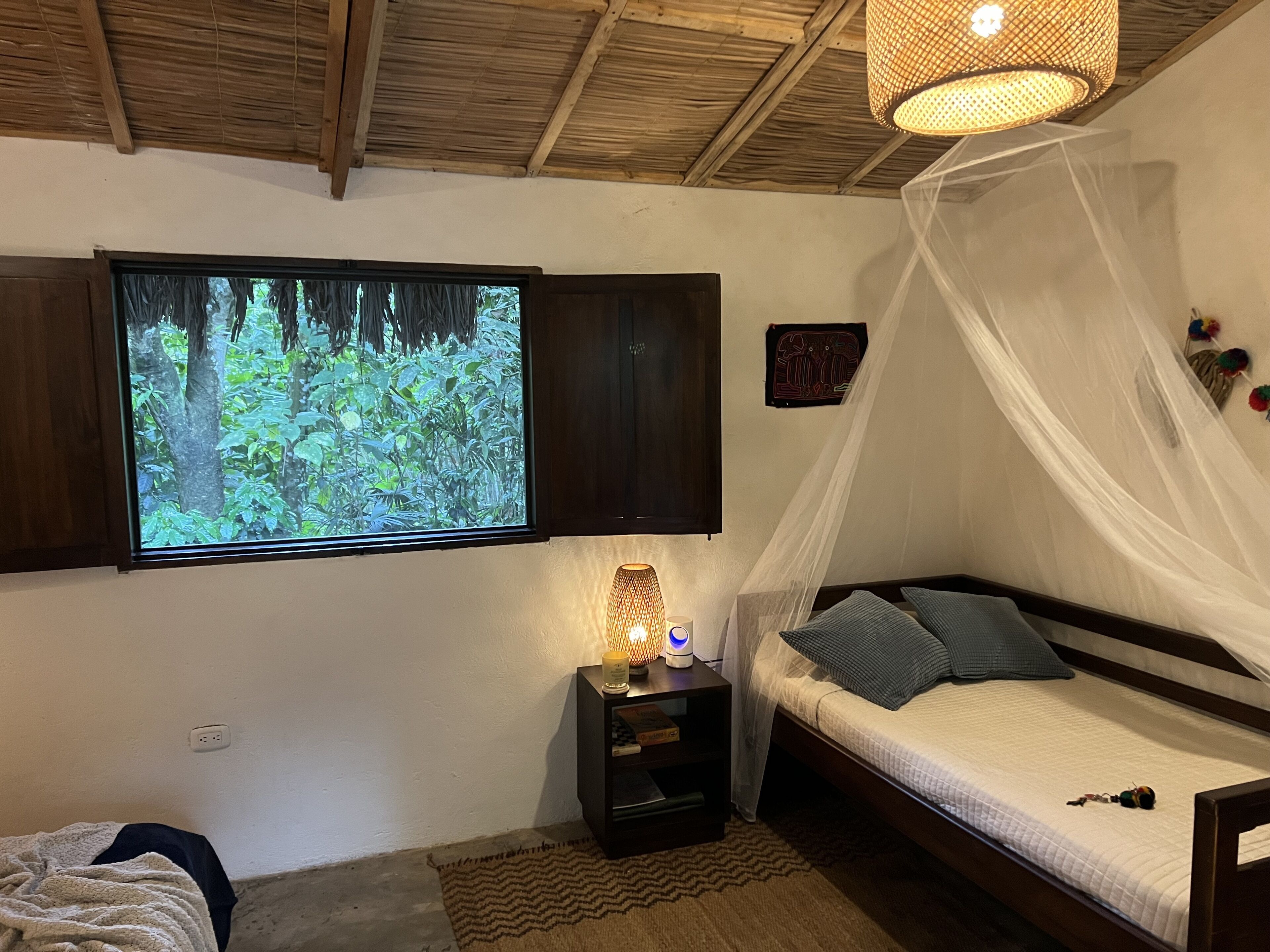 Een slaapkamer met een bed, nachtkastje met lamp, televisie aan de wand en raam met uitzicht op groen.