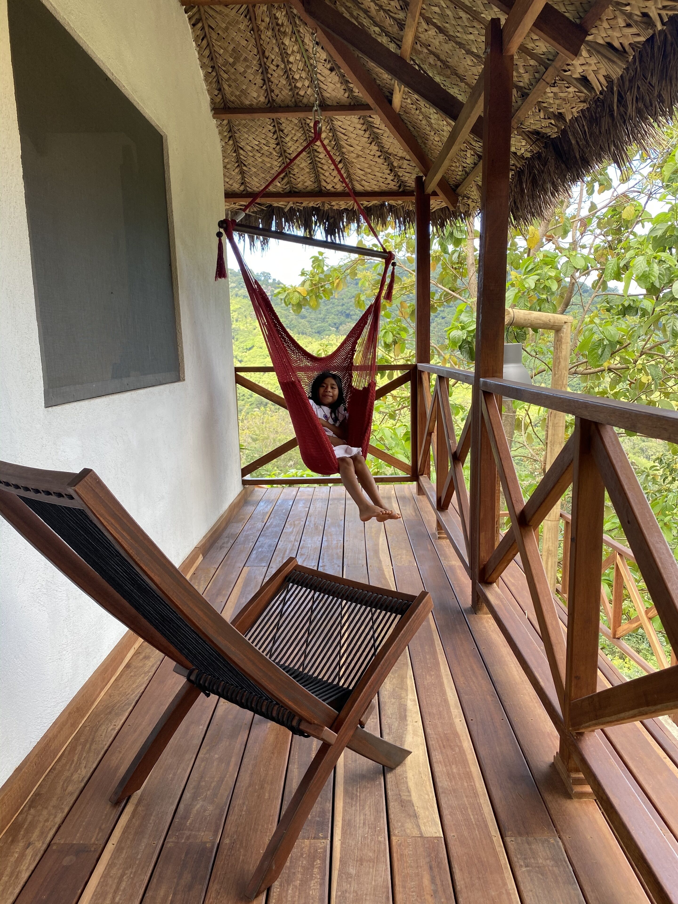 A wooden deck with a hammock, a wooden chair, and a thatched roof structure.