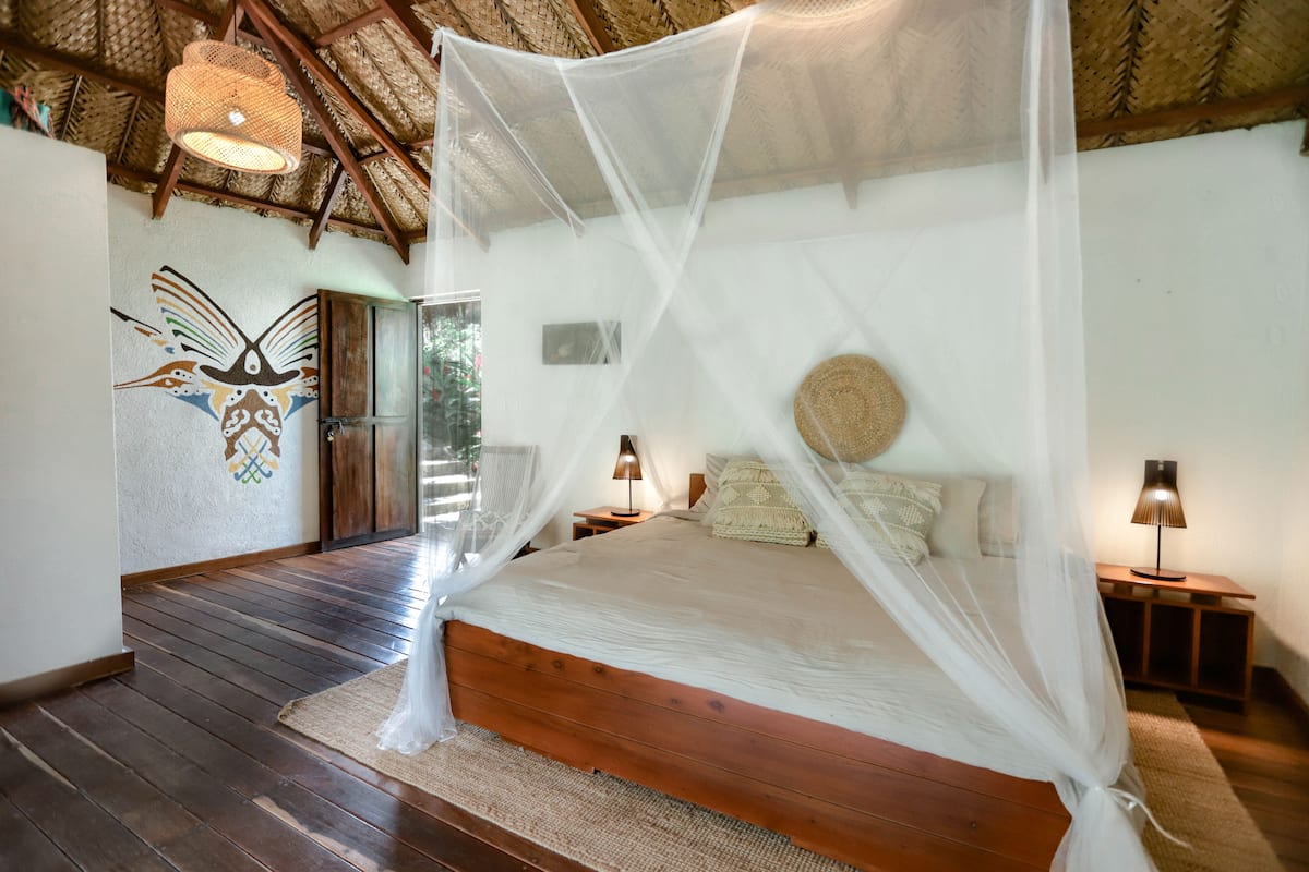 A bedroom with a wooden bed, white canopy, and a woven basket on the headboard.