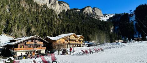 Un edificio de estilo chalet con un telesilla al fondo, rodeado de laderas nevadas y montañas boscosas.