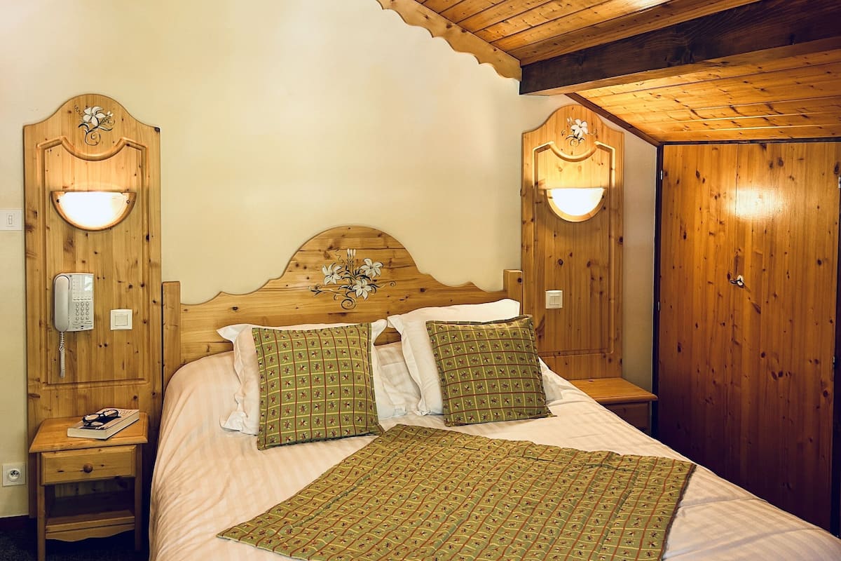 Une chambre à coucher aux murs lambrissés, comprenant un lit, deux tables de chevet, un téléphone et des lampes fixées au mur.